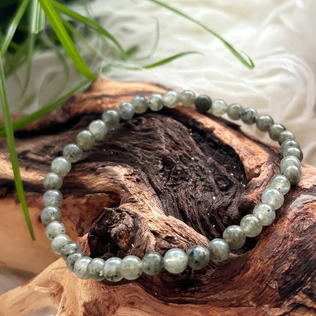 Nahaufnahme eines Labradorit Armbands mit 4 mm Kugelperlen, auf natürlichem Holz dekorativ präsentiert vor weißem Hintergrund